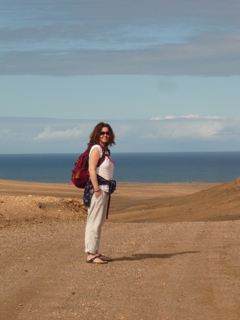 Lucie Stanjurová na pobřeží Fuerteventury — stojí v pouštní krajině s oceánem v pozadí